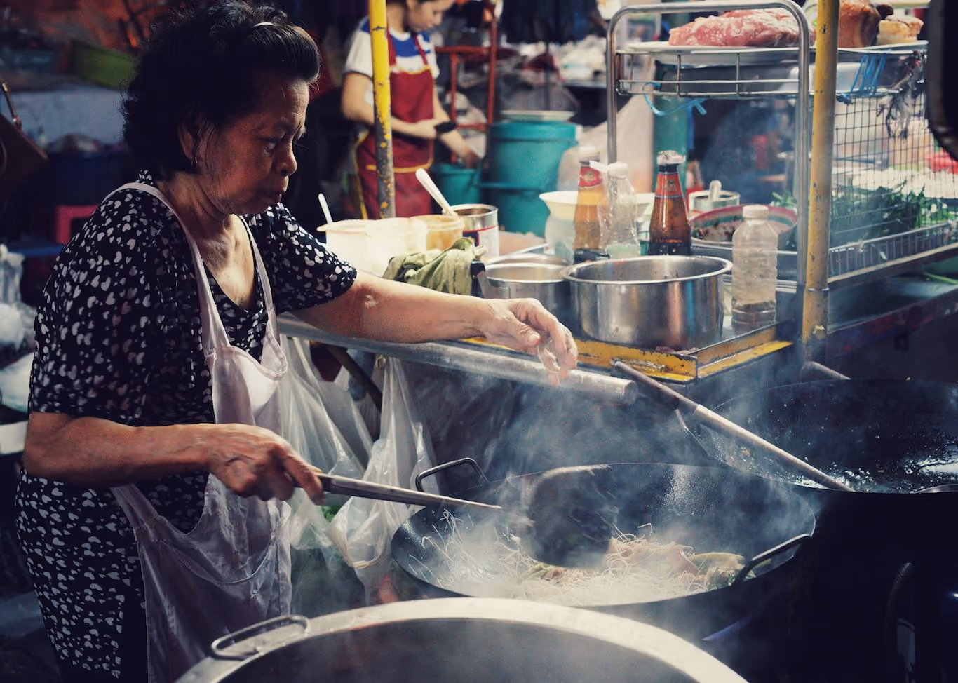 Lady cooking street food at night in Bangkok